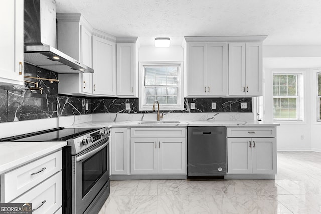 kitchen with wall chimney range hood, decorative backsplash, white cabinets, appliances with stainless steel finishes, and sink