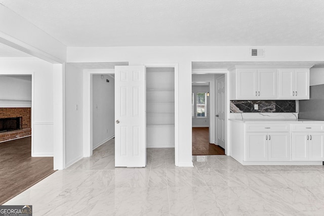 interior space with tasteful backsplash, a textured ceiling, a brick fireplace, white cabinets, and light hardwood / wood-style flooring