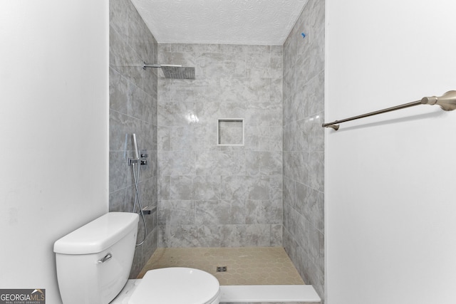 bathroom with toilet, a textured ceiling, and a tile shower