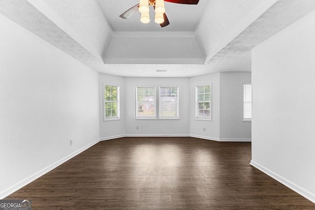 empty room featuring a textured ceiling, a tray ceiling, and dark wood-type flooring