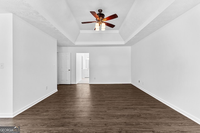 unfurnished room with ceiling fan, a raised ceiling, a textured ceiling, and dark hardwood / wood-style flooring