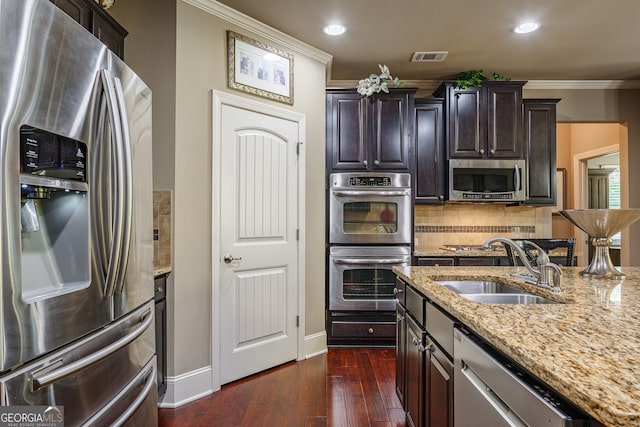 kitchen with appliances with stainless steel finishes, sink, light stone counters, dark wood-type flooring, and crown molding