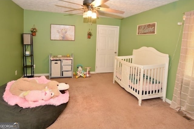 bedroom with a textured ceiling, carpet flooring, a nursery area, and ceiling fan