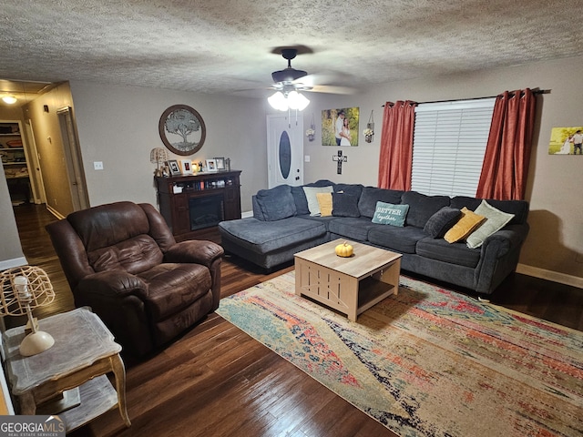 living room featuring dark wood-type flooring, ceiling fan, and a textured ceiling