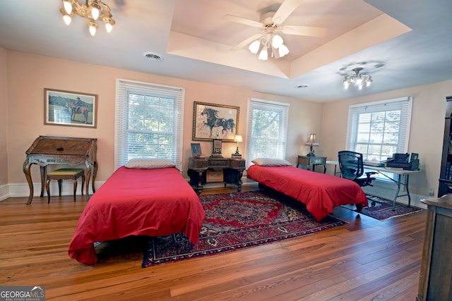 bedroom featuring multiple windows, a tray ceiling, wood-type flooring, and ceiling fan