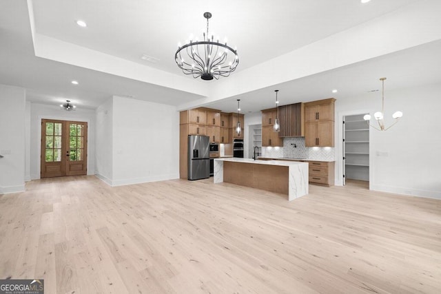 kitchen featuring a spacious island, backsplash, stainless steel fridge, light hardwood / wood-style floors, and decorative light fixtures