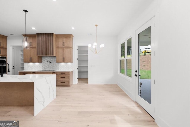 kitchen with backsplash, light stone countertops, light wood-type flooring, black appliances, and pendant lighting