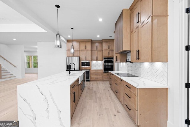 kitchen with light hardwood / wood-style flooring, stainless steel appliances, a large island, decorative light fixtures, and light stone counters