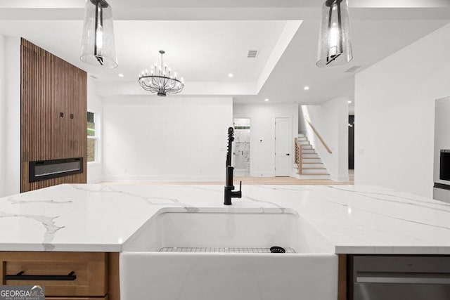 kitchen featuring sink, light stone countertops, a notable chandelier, and decorative light fixtures