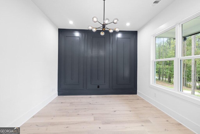 unfurnished dining area featuring a wealth of natural light, light hardwood / wood-style flooring, and a notable chandelier