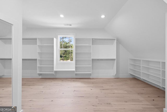 spacious closet with light hardwood / wood-style floors and vaulted ceiling