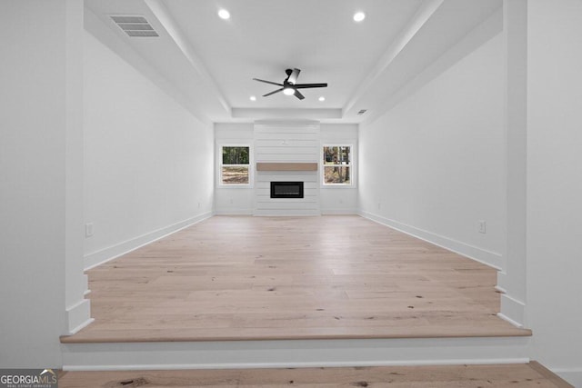 unfurnished living room with light hardwood / wood-style floors, a raised ceiling, and ceiling fan