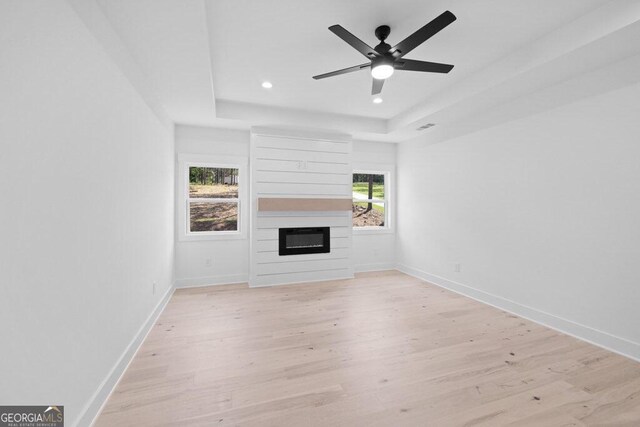 unfurnished living room featuring light hardwood / wood-style floors, a healthy amount of sunlight, ceiling fan, and a raised ceiling