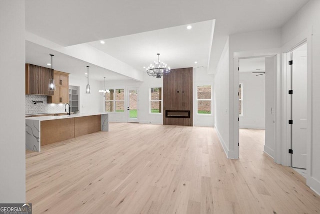 kitchen with a large island, backsplash, pendant lighting, light hardwood / wood-style floors, and sink