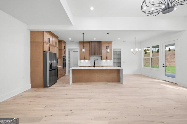 kitchen featuring an island with sink, hanging light fixtures, light hardwood / wood-style flooring, stainless steel fridge, and an inviting chandelier