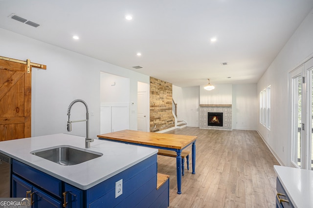 kitchen featuring an island with sink, a barn door, light hardwood / wood-style flooring, a stone fireplace, and blue cabinets