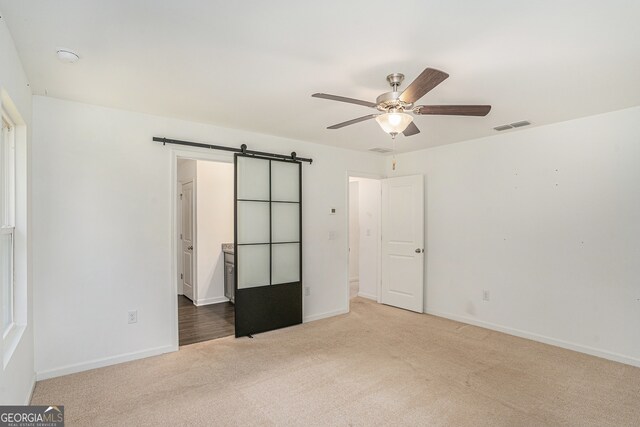 unfurnished bedroom with light colored carpet, ceiling fan, and a barn door