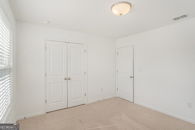 unfurnished bedroom with a closet and light colored carpet