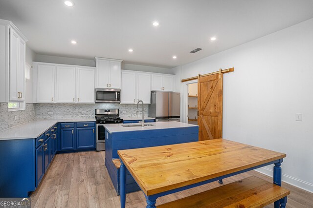 kitchen featuring an island with sink, a barn door, stainless steel appliances, sink, and blue cabinets