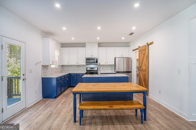 kitchen with white cabinets, a barn door, blue cabinetry, light hardwood / wood-style flooring, and stainless steel appliances