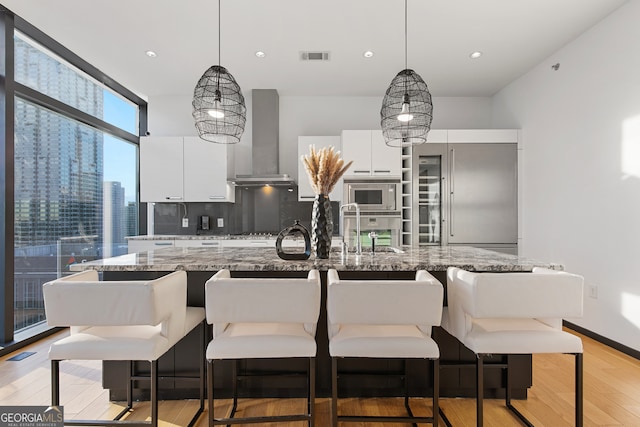 kitchen featuring light hardwood / wood-style flooring, hanging light fixtures, backsplash, white cabinetry, and light stone counters