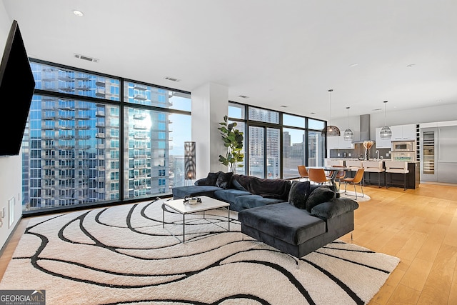 living room featuring light wood-style floors, visible vents, a wall of windows, and a city view