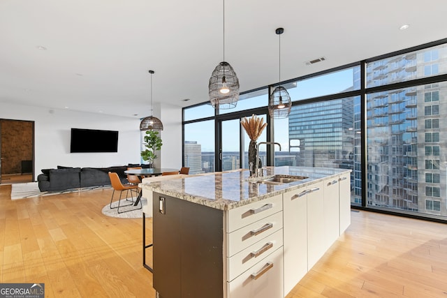 kitchen featuring light hardwood / wood-style flooring, white cabinetry, a kitchen island with sink, and sink