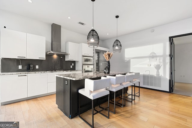 kitchen featuring a center island with sink, tasteful backsplash, wall chimney range hood, white cabinets, and appliances with stainless steel finishes