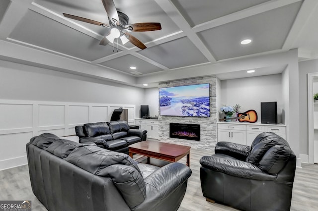 living room featuring ceiling fan, light wood-type flooring, beamed ceiling, a stone fireplace, and coffered ceiling