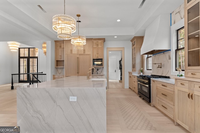 kitchen featuring premium range hood, a spacious island, a chandelier, light brown cabinets, and range with two ovens