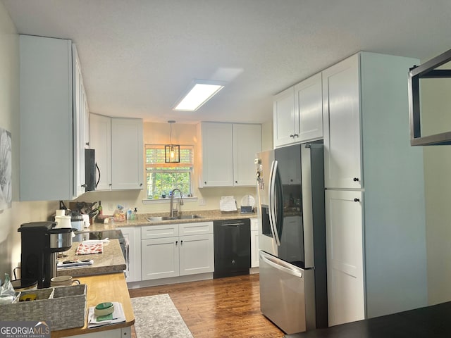 kitchen featuring black appliances, sink, pendant lighting, white cabinets, and light hardwood / wood-style flooring