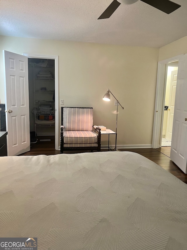 unfurnished bedroom featuring ceiling fan, a textured ceiling, a spacious closet, dark hardwood / wood-style floors, and a closet