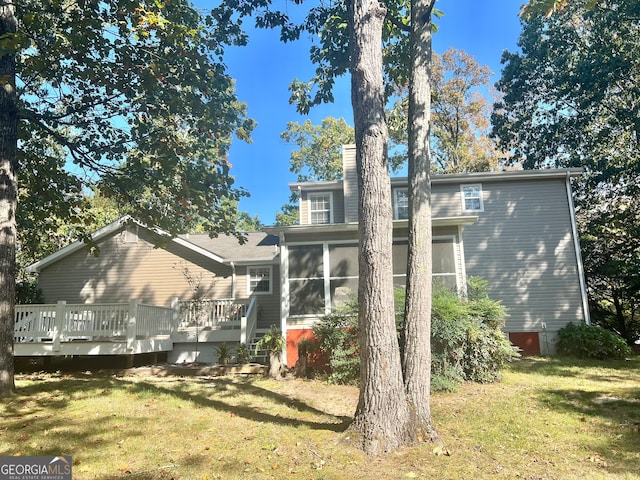 rear view of property featuring a sunroom, a deck, and a lawn