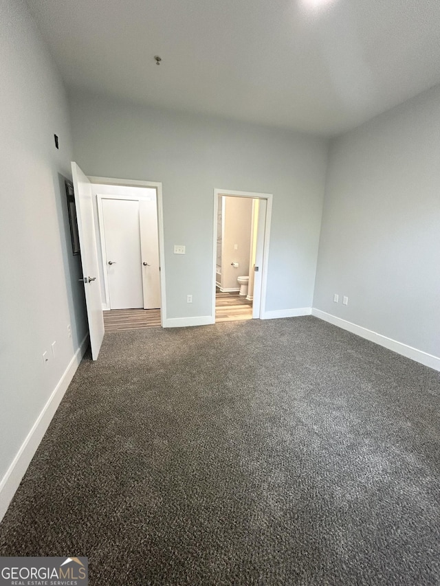 unfurnished bedroom with ensuite bath and dark colored carpet