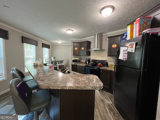 kitchen featuring wall chimney range hood, dark hardwood / wood-style flooring, a kitchen bar, black appliances, and crown molding