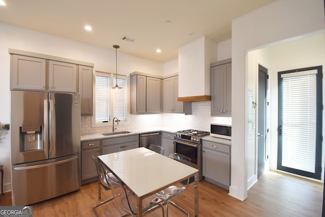 kitchen featuring hanging light fixtures, light hardwood / wood-style flooring, sink, gray cabinetry, and stainless steel appliances