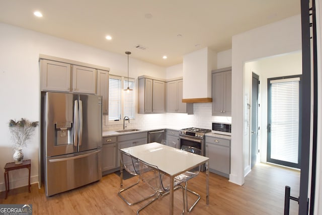 kitchen with hanging light fixtures, appliances with stainless steel finishes, light hardwood / wood-style flooring, gray cabinets, and sink