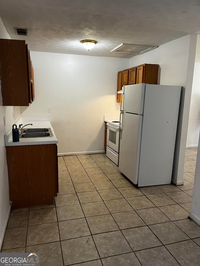 kitchen with white appliances, light tile patterned floors, a textured ceiling, and sink