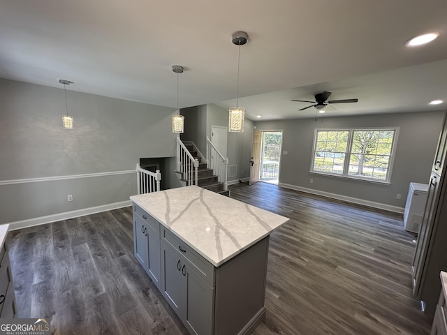 kitchen featuring gray cabinets, dark hardwood / wood-style floors, pendant lighting, a center island, and light stone countertops