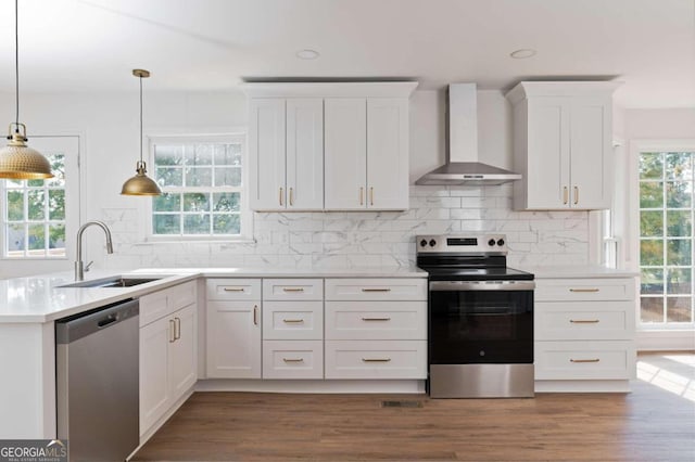 kitchen with wall chimney exhaust hood, sink, decorative light fixtures, white cabinetry, and appliances with stainless steel finishes