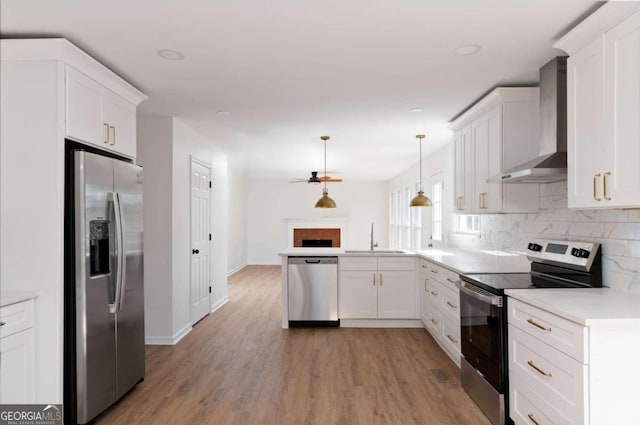 kitchen featuring sink, ceiling fan, stainless steel appliances, wall chimney exhaust hood, and pendant lighting