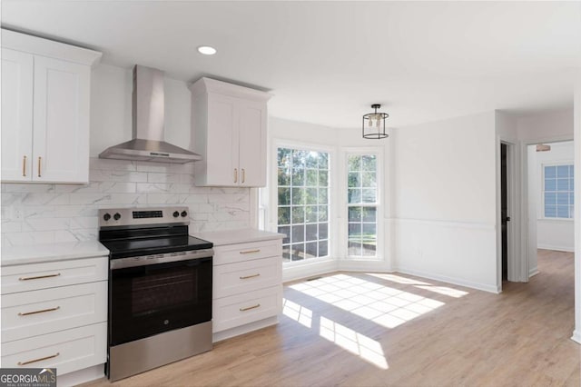 kitchen featuring wall chimney range hood, stainless steel electric stove, white cabinetry, light hardwood / wood-style floors, and tasteful backsplash