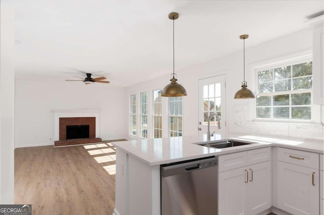 kitchen with white cabinetry, stainless steel dishwasher, a brick fireplace, decorative light fixtures, and sink