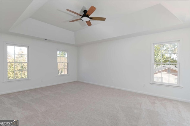 empty room with light carpet, a tray ceiling, and ceiling fan