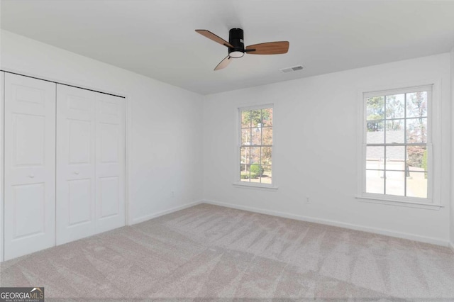 unfurnished bedroom featuring ceiling fan, multiple windows, and light colored carpet