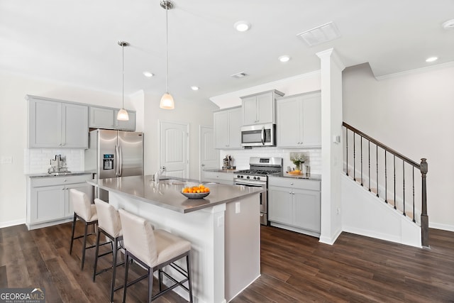 kitchen featuring dark wood-type flooring, appliances with stainless steel finishes, a center island with sink, a kitchen bar, and decorative light fixtures