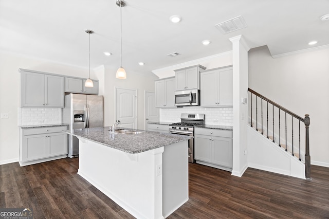 kitchen featuring an island with sink, backsplash, stainless steel appliances, decorative light fixtures, and dark wood-type flooring