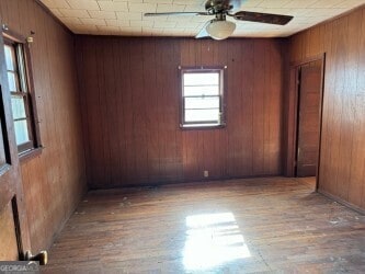 spare room featuring hardwood / wood-style floors, ceiling fan, and wooden walls