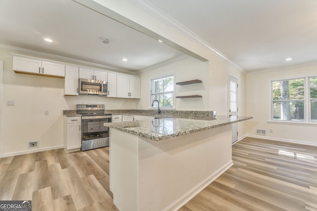 kitchen with appliances with stainless steel finishes, white cabinetry, light stone counters, and light hardwood / wood-style floors