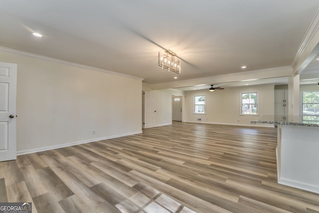 unfurnished living room featuring ornamental molding, ceiling fan with notable chandelier, and light wood-type flooring